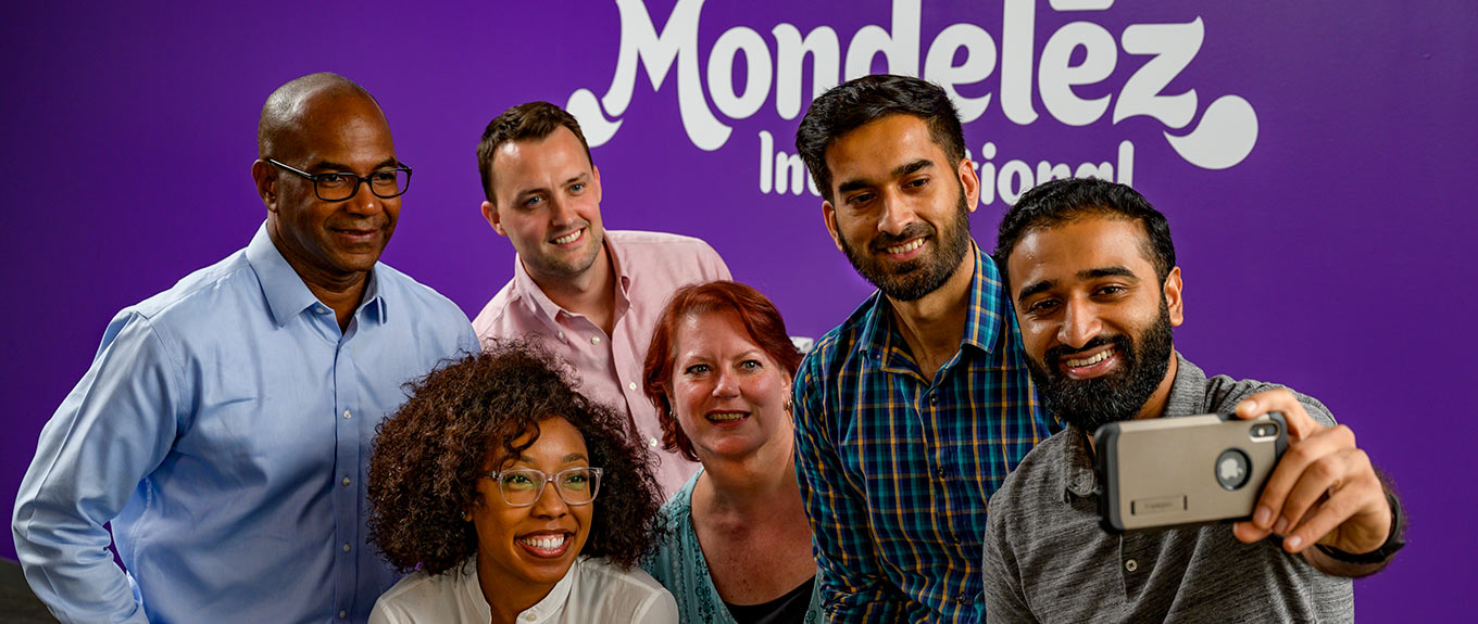 3 multicultural Mondelez staff sitting around a laptop smiling and talking.