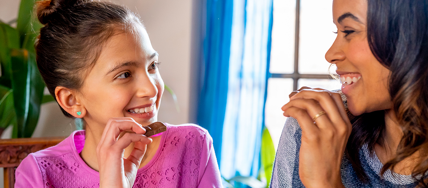 Mother and daughter smiling at each other while holding chocolate snacks.