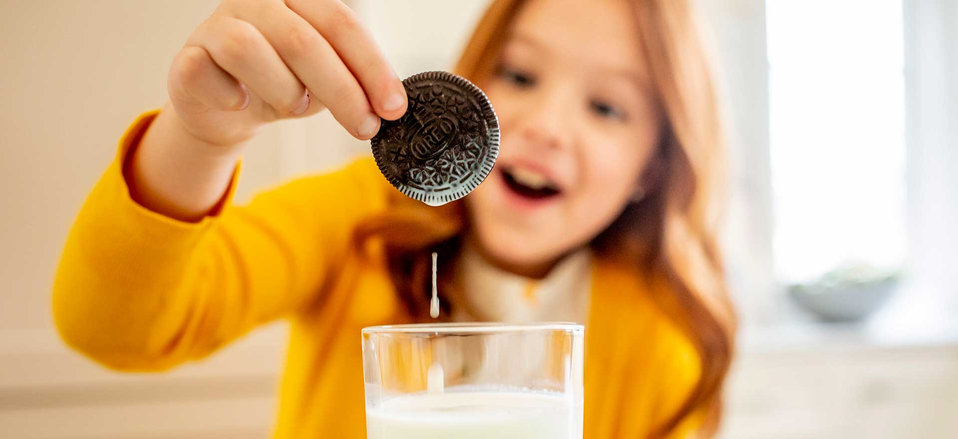 Young girl excitedly dunking an Oreo cookie into milk.