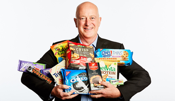 Mondelēz CEO Dirk Van de Put holding a wide range of Mondelez products in his hands while he smiles.