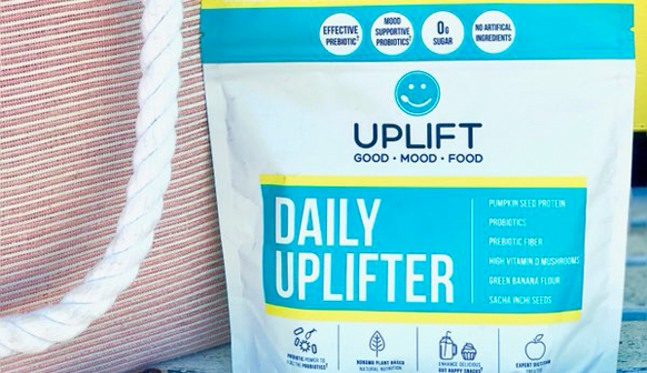 Uplift Daily Uplifter package leaning on a red and white striped purse